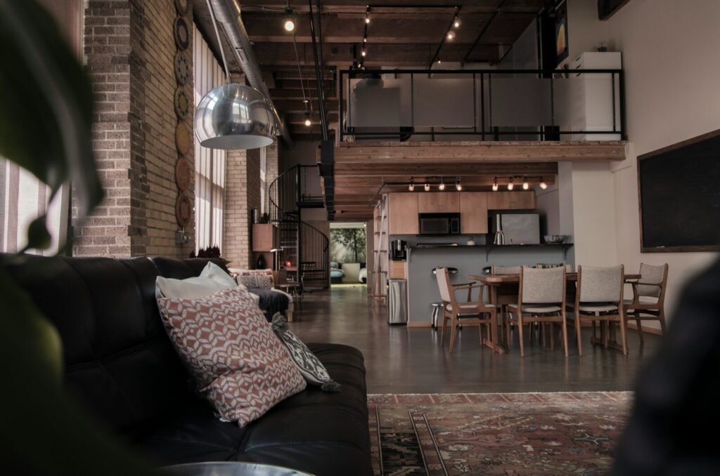 A spacious industrial loft with a black leather sofa, dining area, and mezzanine level